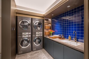 Uma lavanderia moderna com quatro máquinas de lavar industriais LG, uma pia com artigos de higiene e um revestimento de azulejos azuis.