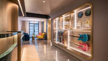 A modern hotel lobby with a marble floor, seating area with chairs, and a wall display of musical instruments.