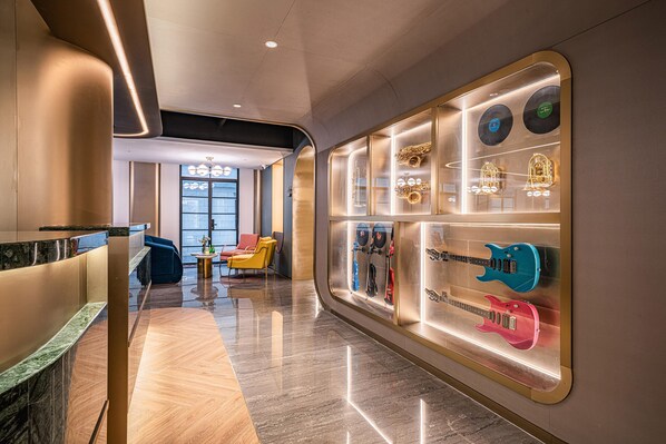 A modern hotel lobby with a marble floor, seating area with chairs, and a wall display of musical instruments. - Manxin Hotel Yantai Binhai Plaza (Yantai)