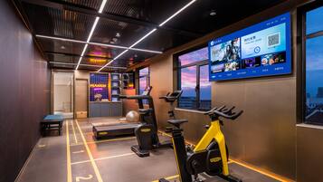 A modern gym with exercise equipment, a digital screen displaying information, and a city view through large windows.