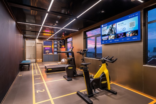 Ein modernes Fitnessstudio mit Trainingsgeräten, einem digitalen Bildschirm und Blick auf die Stadt durch große Fenster.