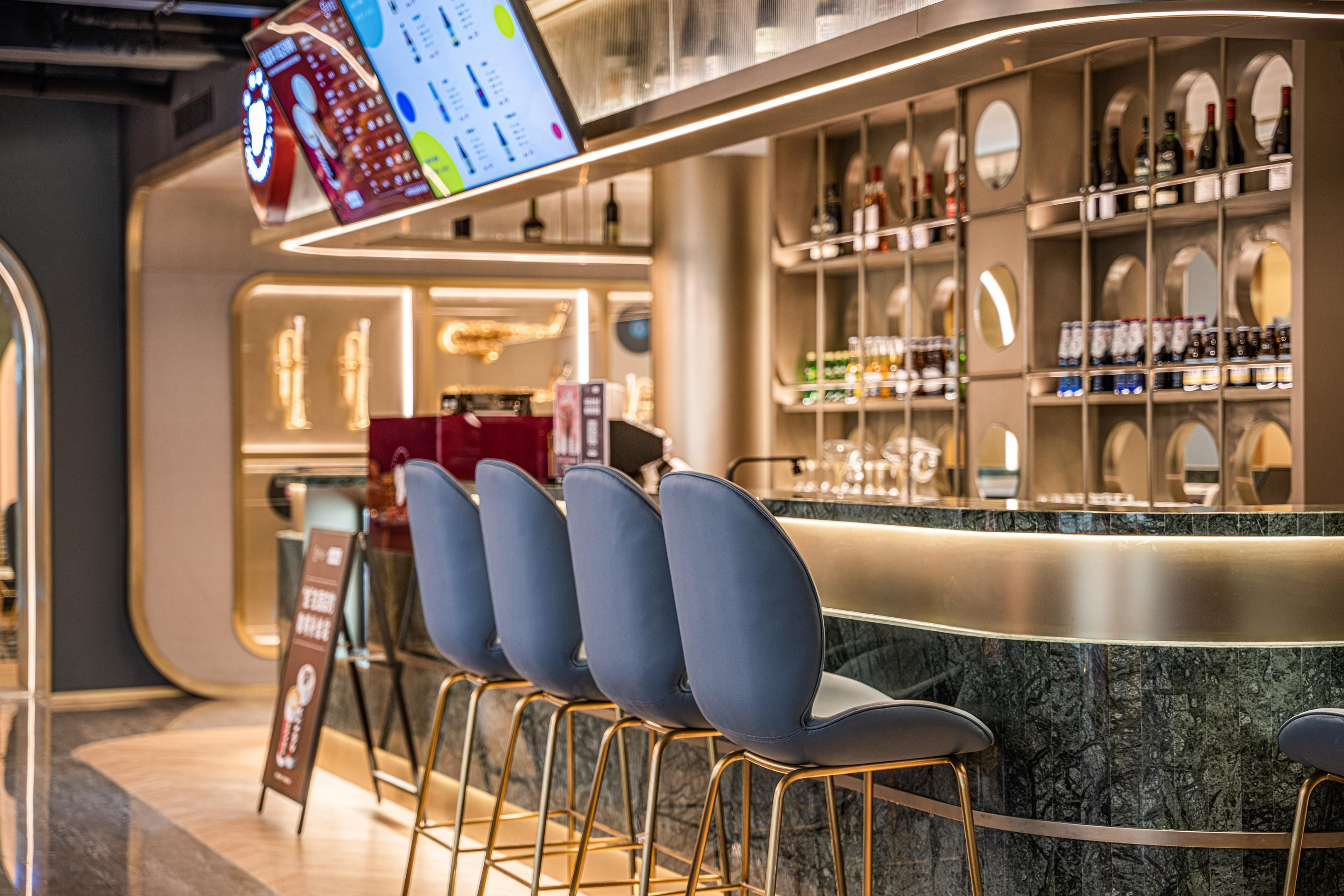 Zona de bar con mostrador, estanterías llenas de botellas y una pantalla de menú.