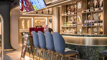 Zona de bar con mostrador, estanterías llenas de botellas y una pantalla de menú.