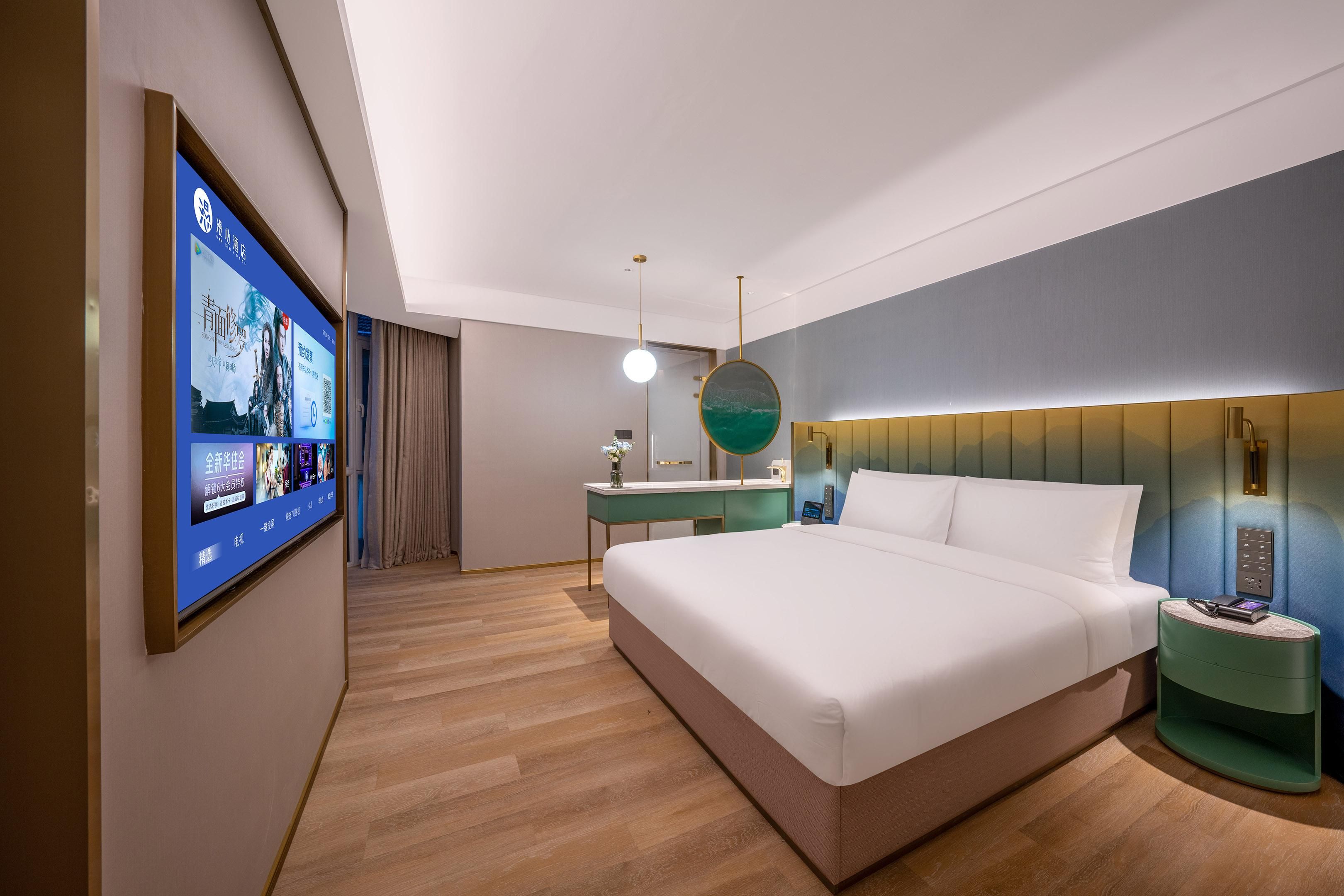 A modern hotel room with a large bed, a desk, a vanity, and a television displaying a menu.