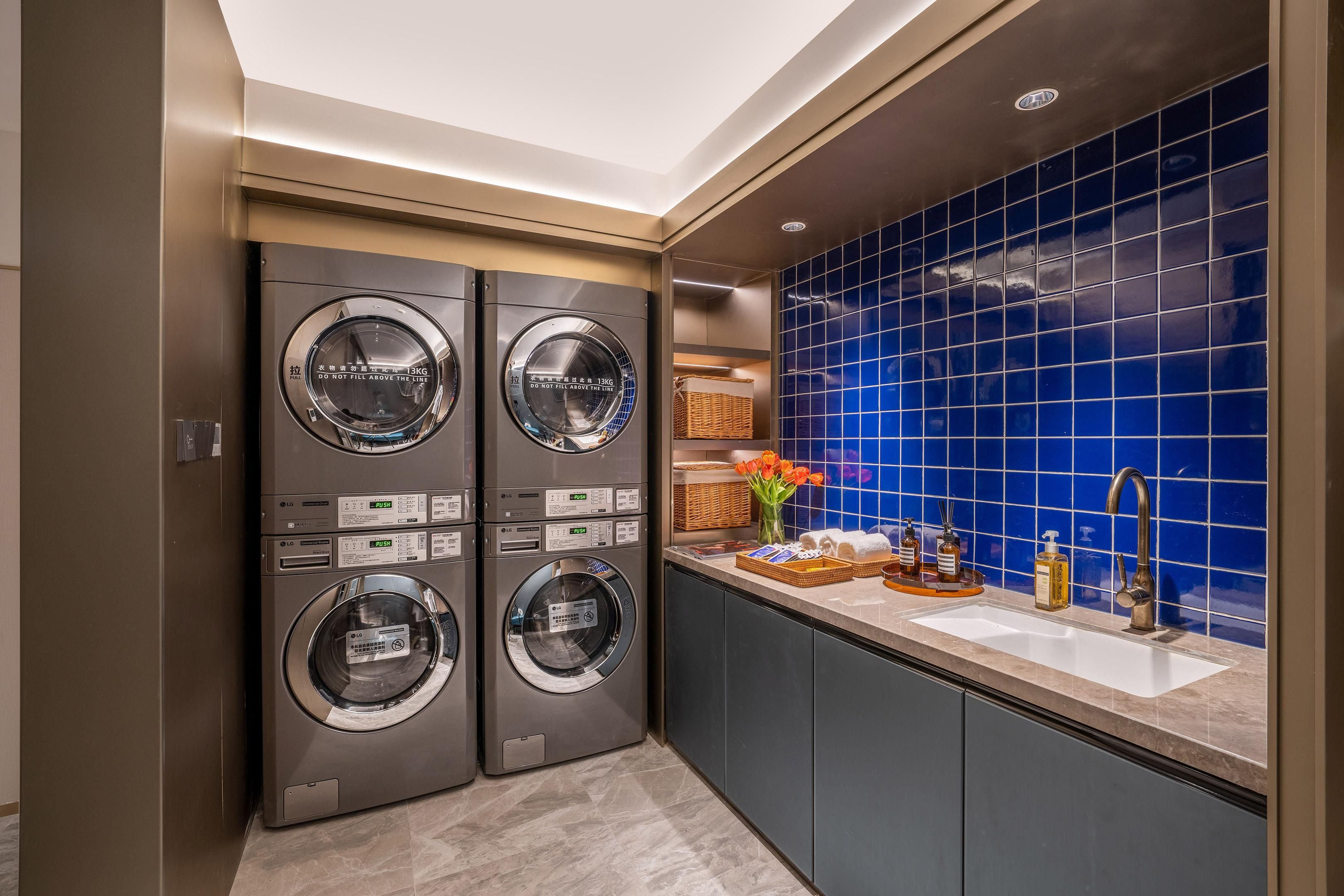 A laundry area with four LG commercial washers, a sink with toiletries, and a blue-tiled backsplash.