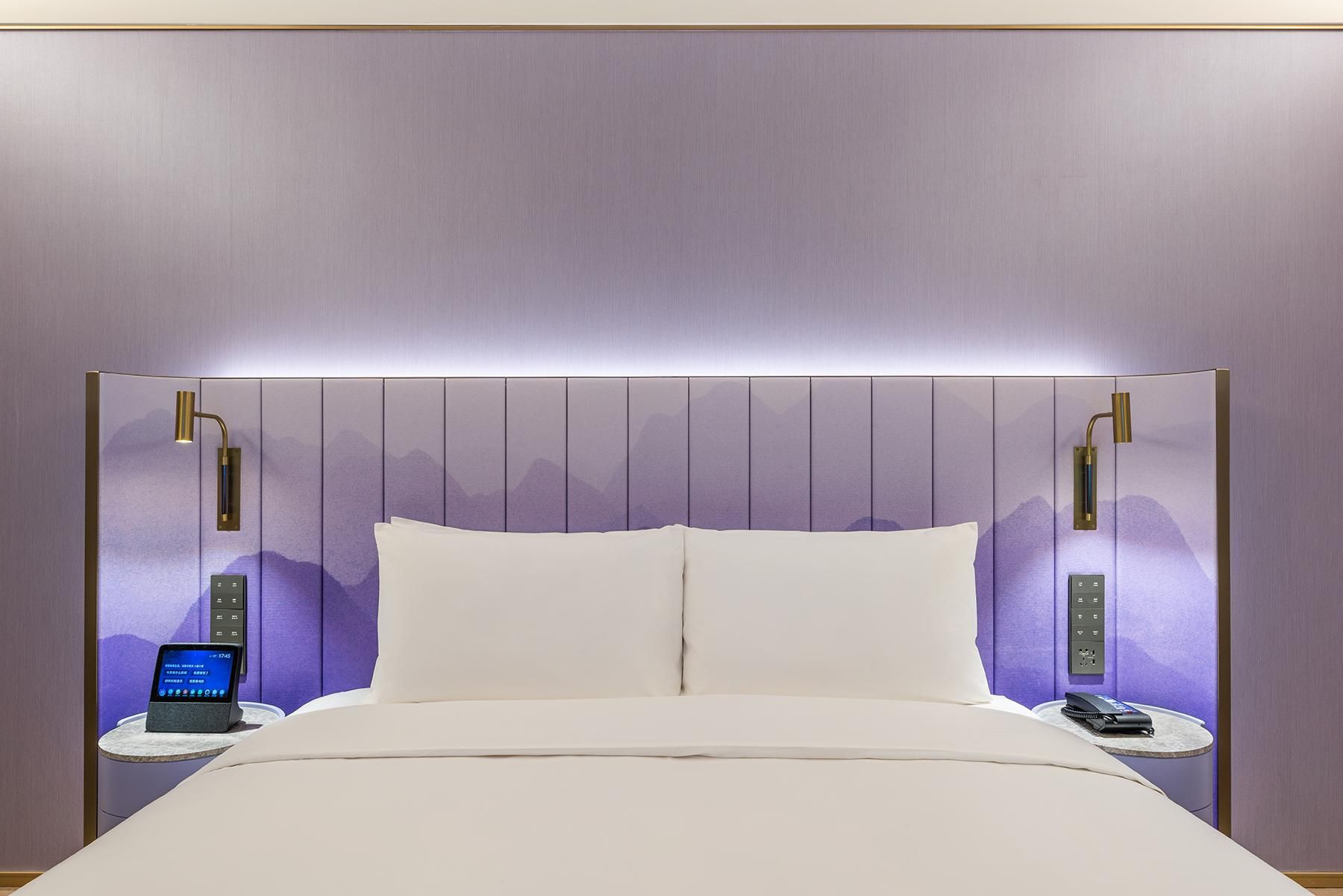 Habitación de hotel con una cama, dos mesitas de noche, un panel de control y una pared con un diseño de montaña.