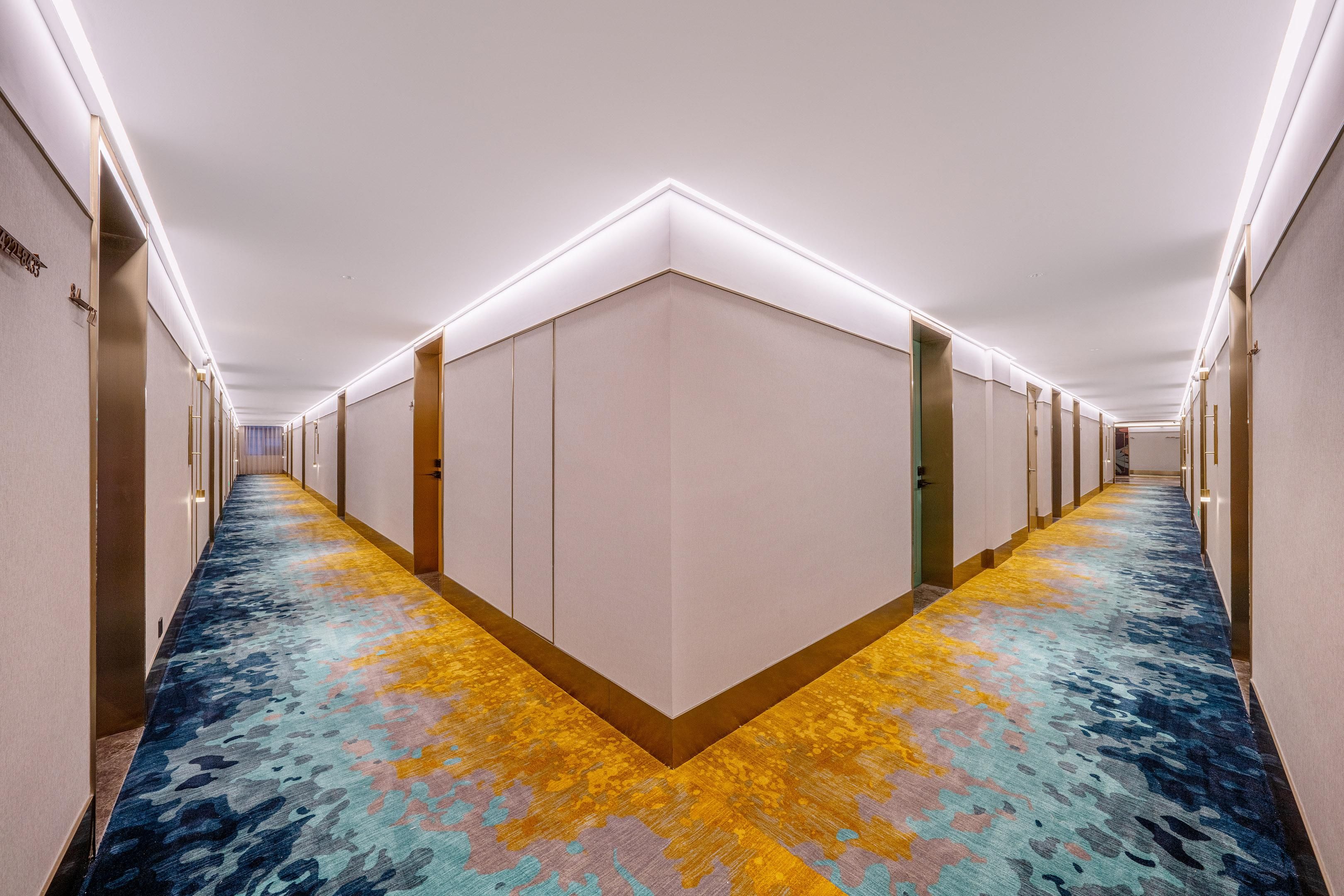 A hotel corridor with a patterned carpet, doors, and a ceiling with recessed lighting.