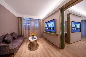 A modern hotel room with a sofa, a small table with a vase, and two large digital screens displaying content. - Manxin Hotel Yantai Binhai Plaza (Yantai)