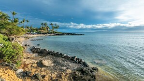 A coastal beach with a rocky shoreline, palm trees, and a building with a view of the ocean. - Island Surf 614 2 Bedroom Apts (Kihei)