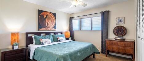 A bedroom with a bed, nightstands, a ceiling fan, a window with curtains, and a wooden dresser.