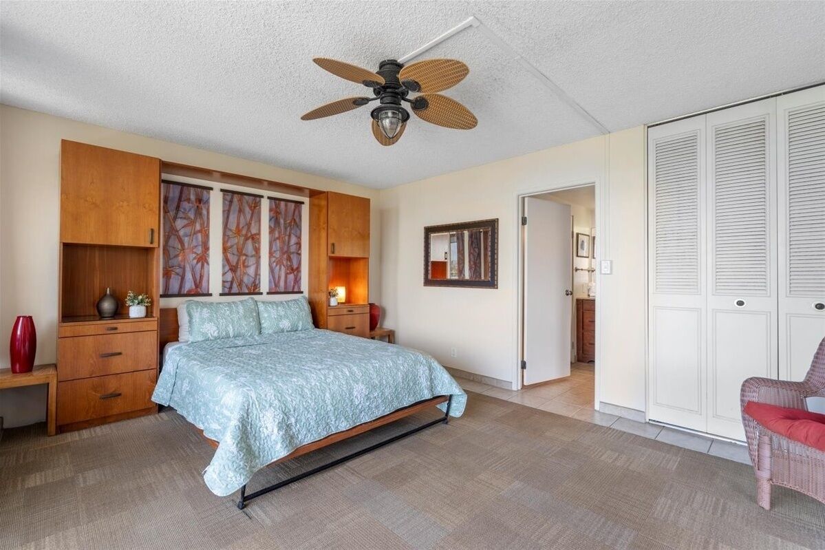 A bedroom with a bed, wooden wardrobe, ceiling fan, and a red chair.