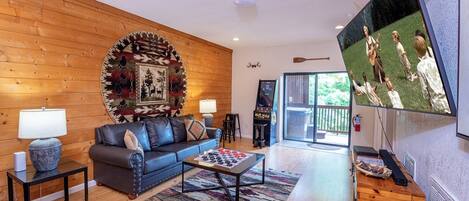 A cozy living room with a wooden wall, a sofa, a coffee table, a TV, and a fireplace.