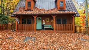 Une cabane avec une façade en bois, deux lucarnes, une porte verte et une véranda avec un banc.