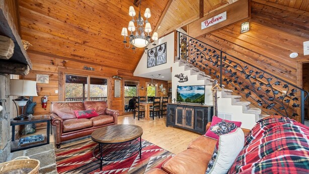 L’intérieur chaleureux d’un chalet en bois comprend un canapé en cuir, un coin repas et un escalier orné de motifs d’oiseaux.