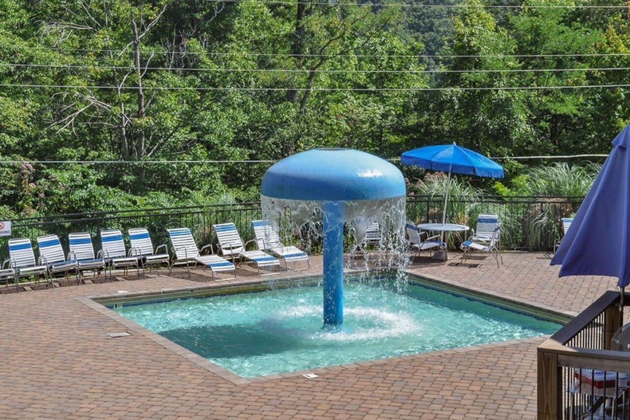 A pool with a blue water feature, surrounded by lounge chairs and umbrellas.