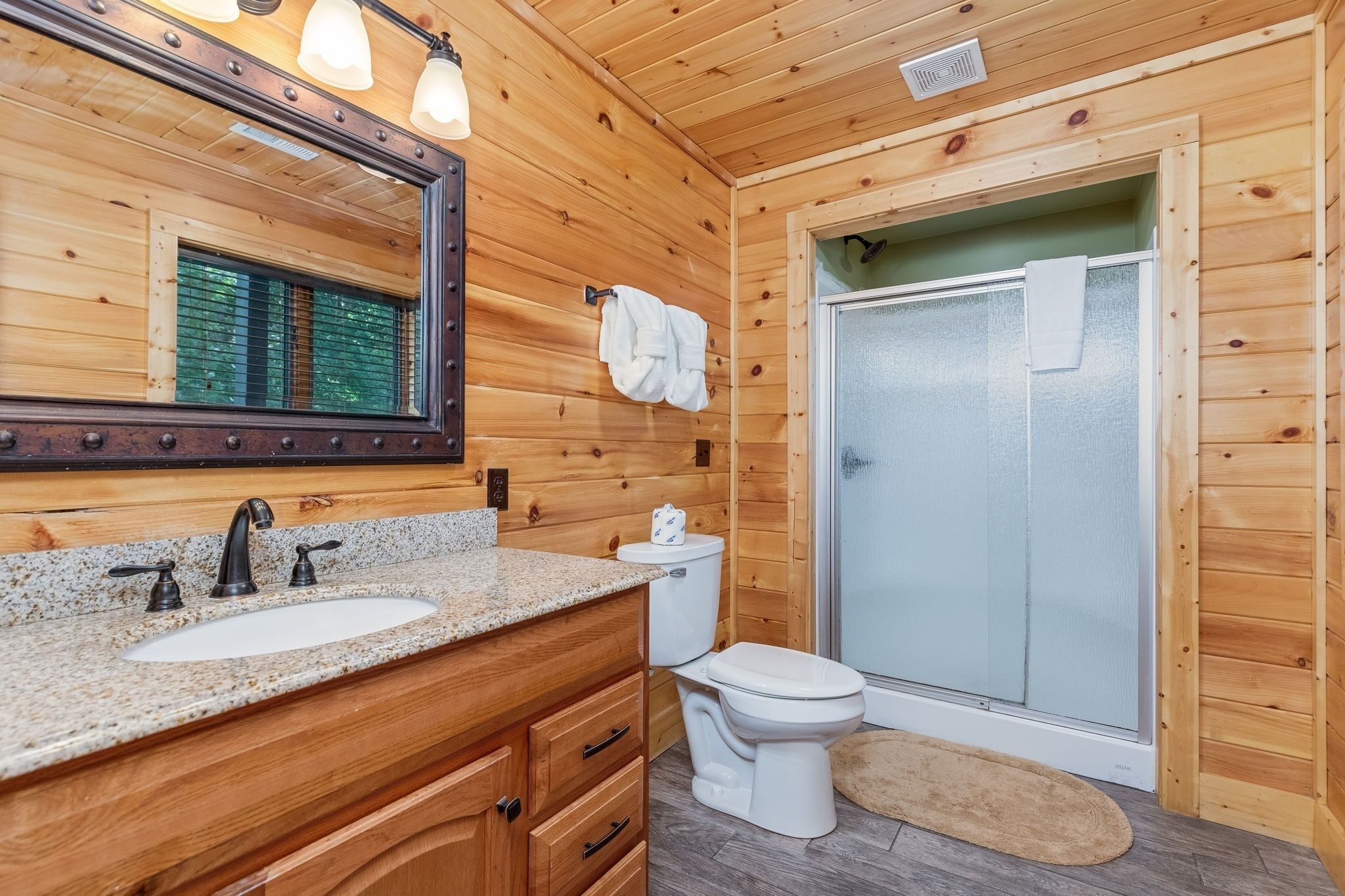 A wooden cabin bathroom with a granite sink, a toilet, a shower, and a large mirror.