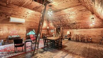 Une pièce mansardée chaleureuse avec des murs en bois, une table à manger avec des chaises, une échelle et un lustre.