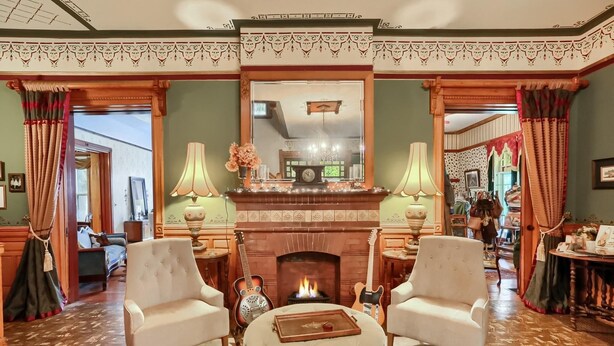 Una habitación tradicional con chimenea, dos sillones, un reposapiés redondo y un espejo sobre la chimenea.