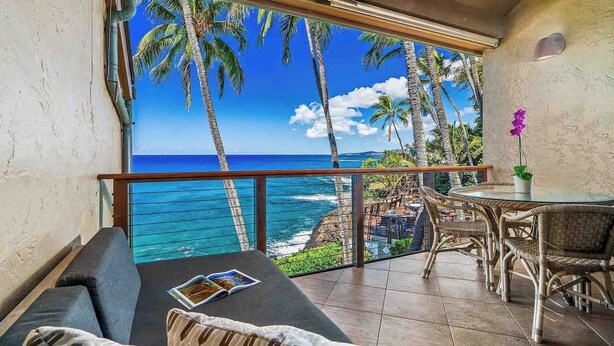 Un balcón con vista al océano, una zona de comedor con muebles de mimbre y una revista en el sofá.