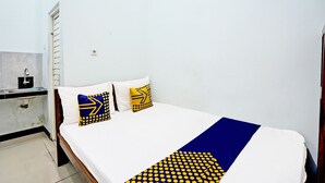 A bedroom with a bed, two pillows, a blue and yellow blanket, and a small kitchenette area with a sink and a coffee machine.