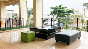 A spacious balcony with a black table and two ottomans, one green and one black, on a tiled floor.