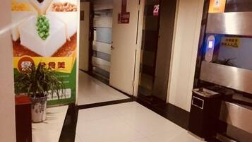 Un pasillo de hotel con una recepción, una planta y un contenedor de basura.