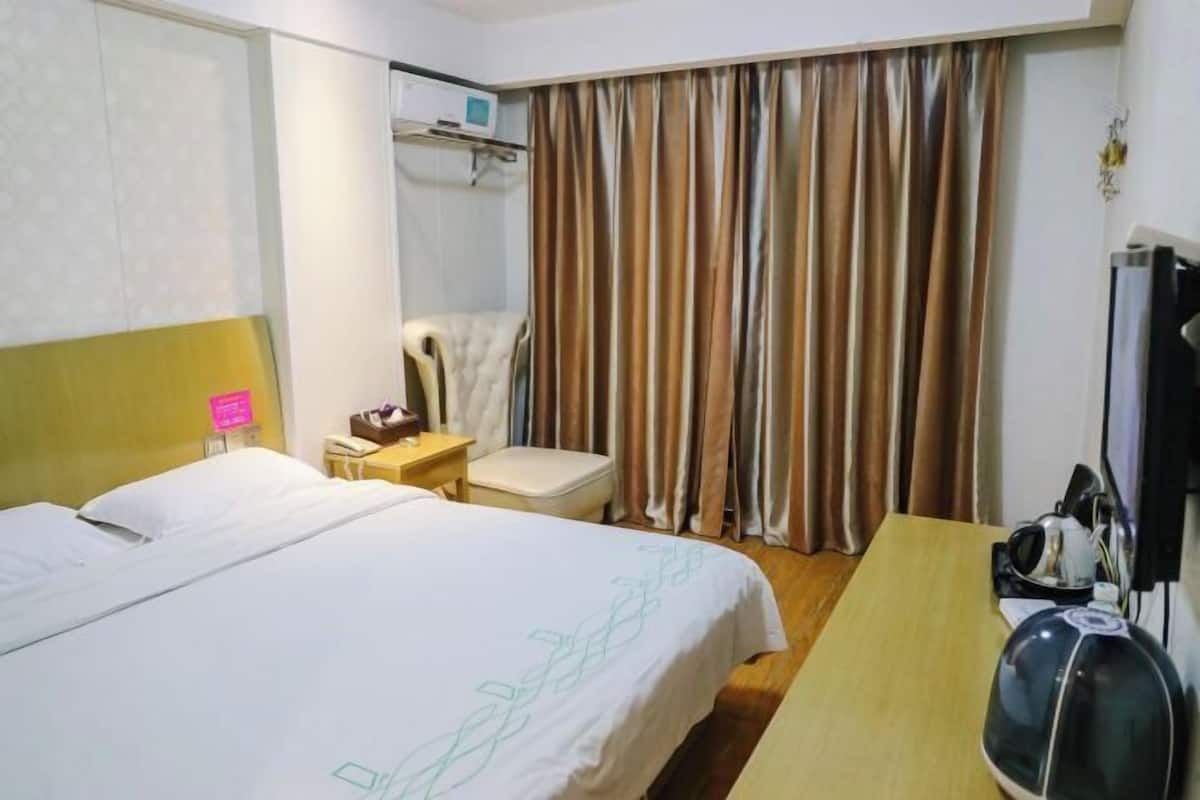 A hotel room with a bed, a desk, a chair, a television, and a window with curtains.