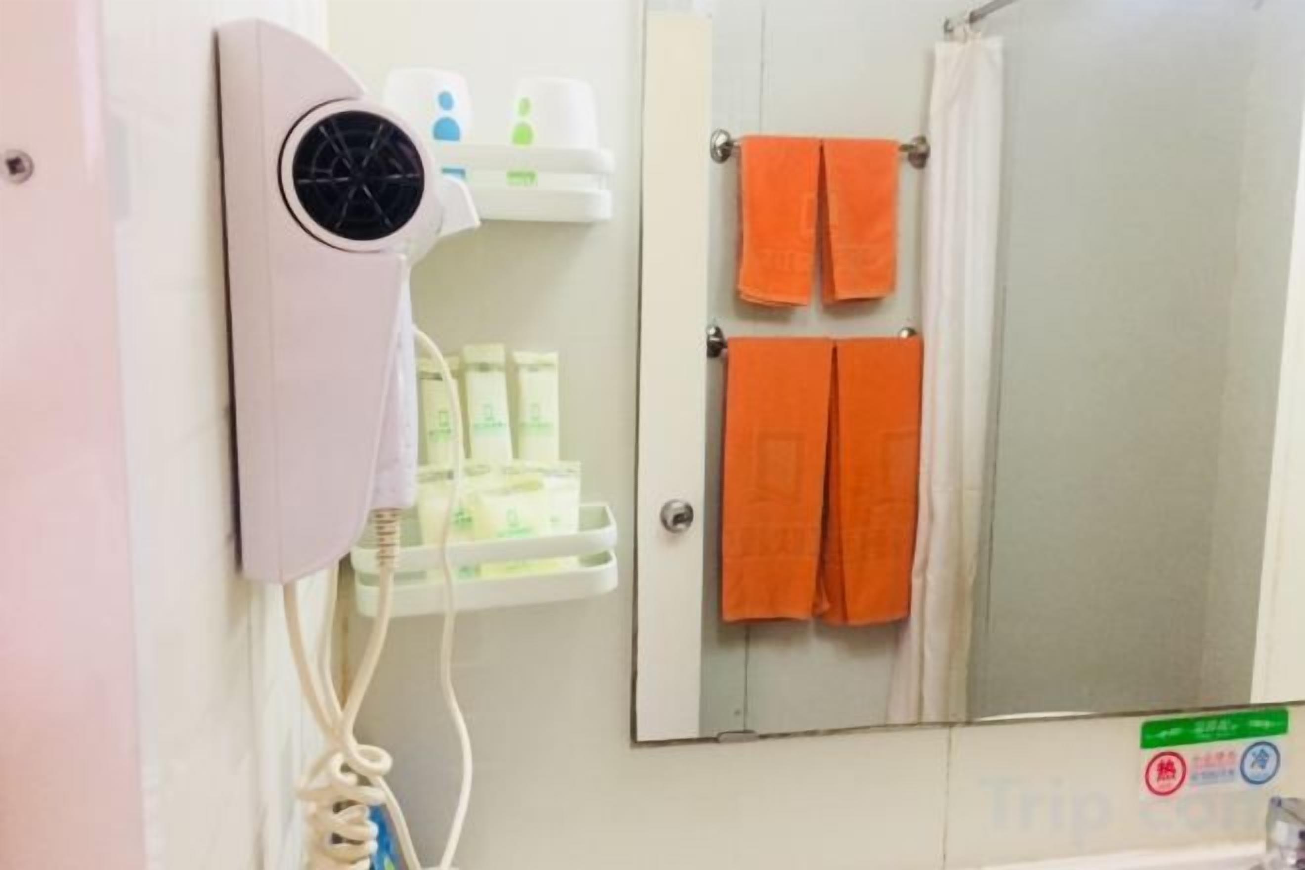 A bathroom with a hairdryer, a shelf with toiletries, and two towels hanging on a rack.