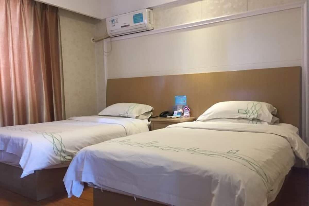 A hotel room with two beds, a nightstand, an air conditioning unit, and a curtain.