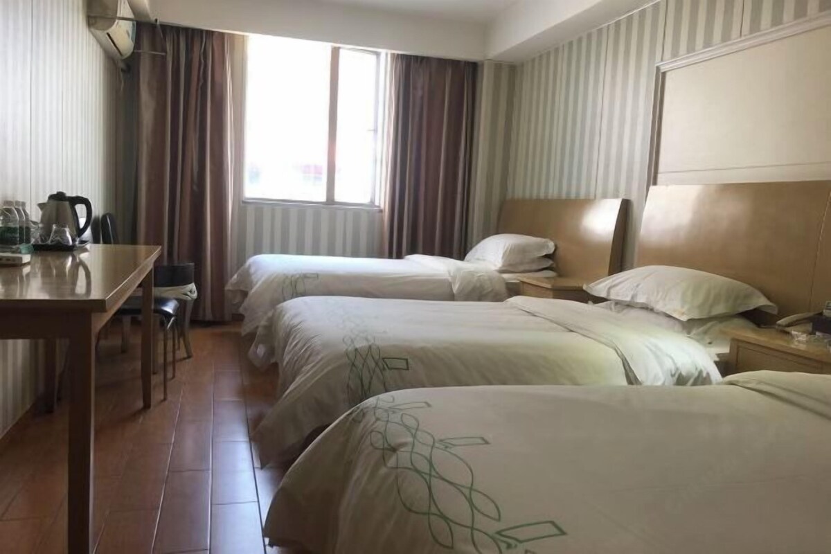 A hotel room with two beds, a desk with a kettle, and a window with curtains.