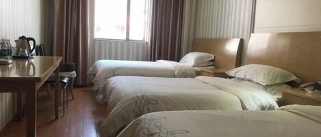 A hotel room with two beds, a desk with a kettle, and a window with curtains.