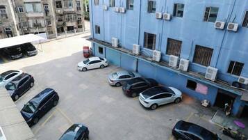 A parking lot with several cars, a blue building with air conditioning units, and a covered area.