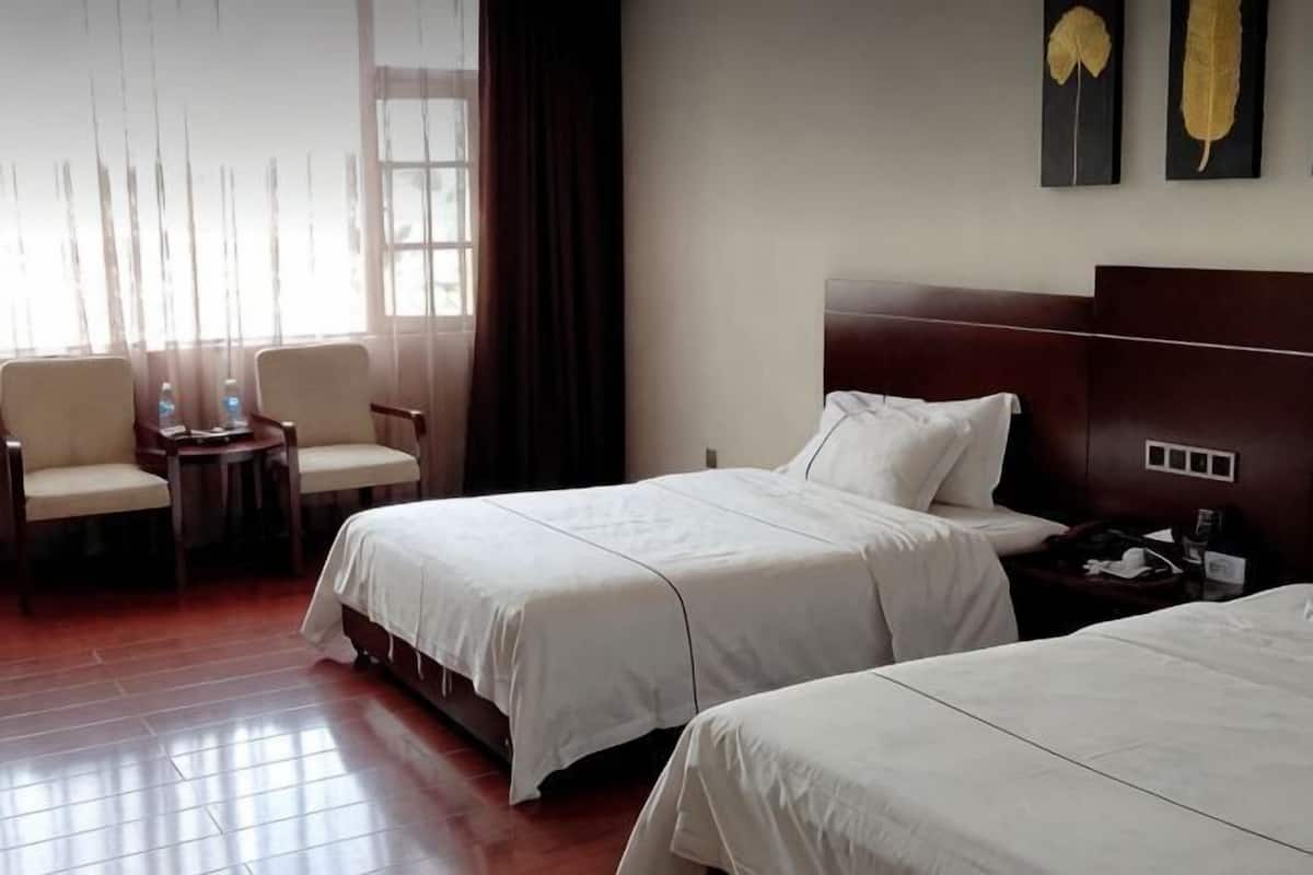 A hotel room with two beds, a desk, chairs, and a window with curtains.