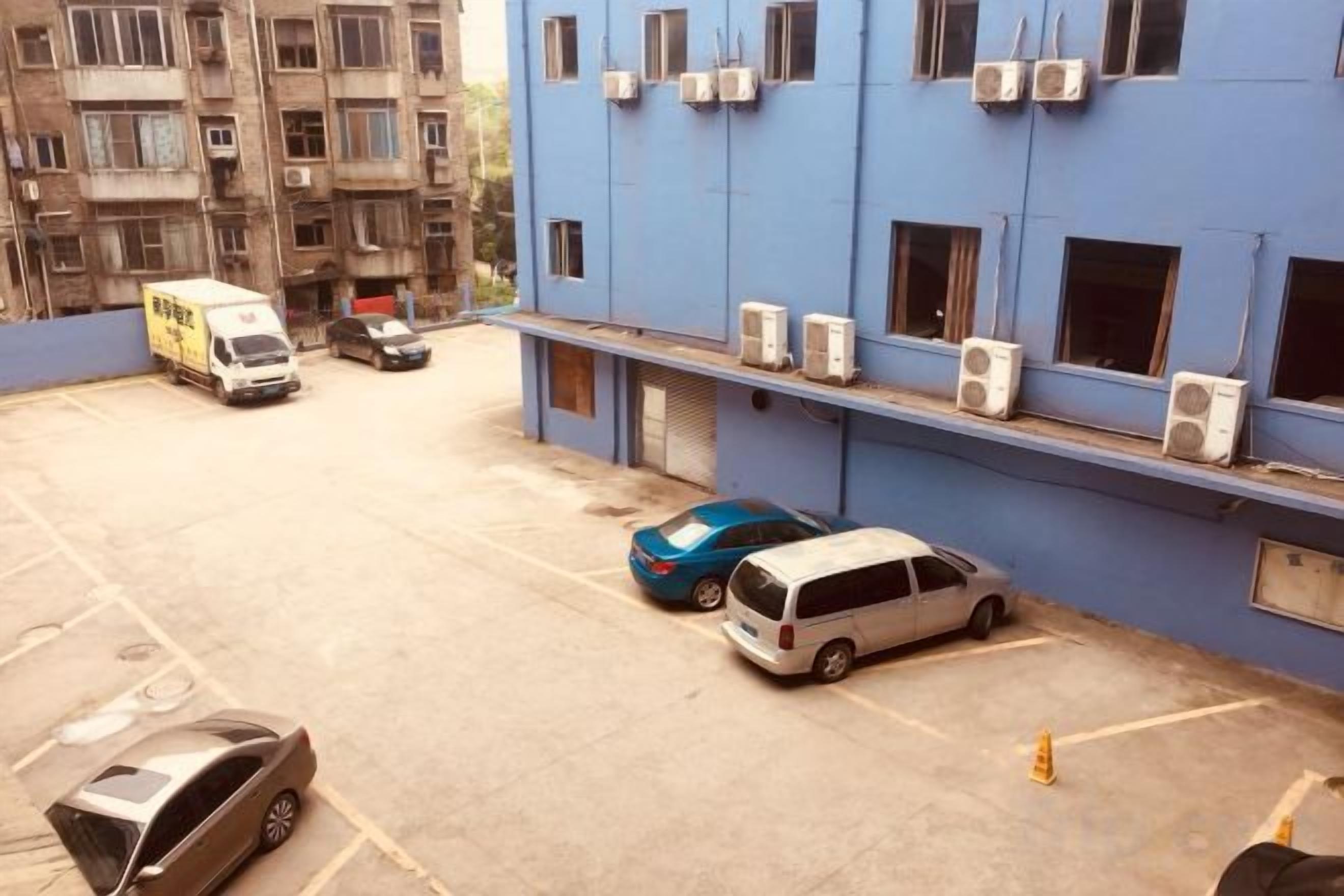 A parking area with several vehicles, including a white van, a blue car, and a silver car.
