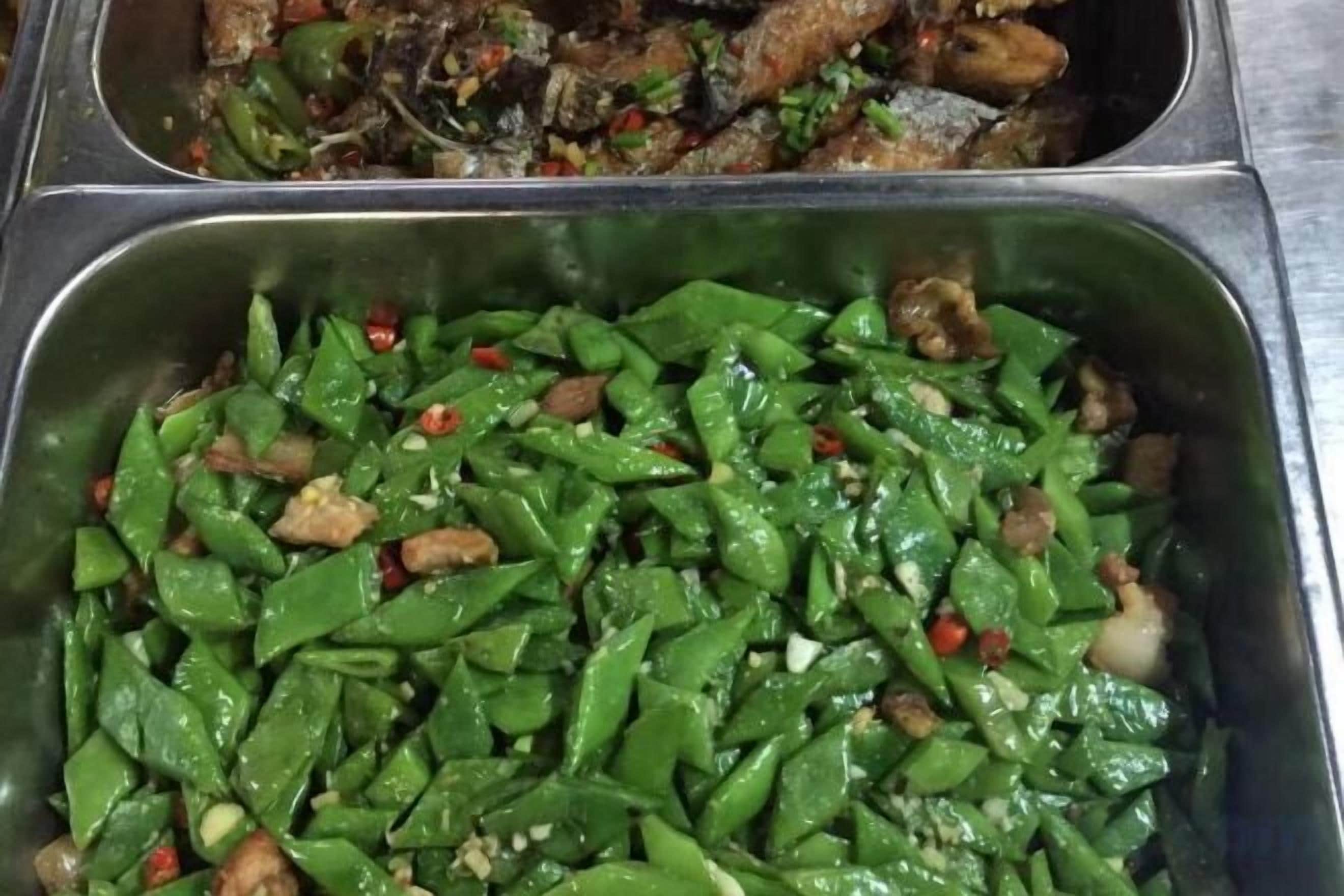 Un buffet in acciaio inossidabile con diversi piatti, tra cui verdure saltate e carne.