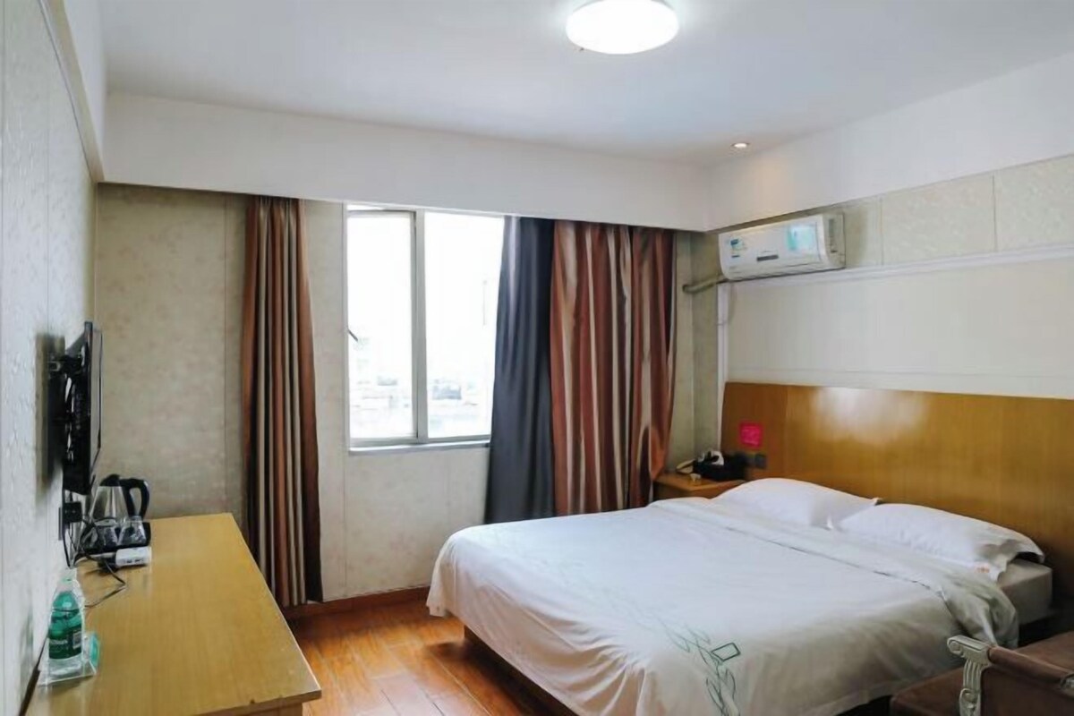 A hotel room with a bed, a desk with a kettle, a water bottle, and a TV.