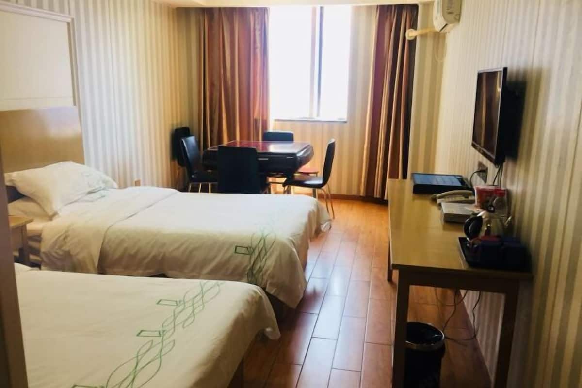 A hotel room with two beds, a desk with a chair, a television, and a window with curtains.