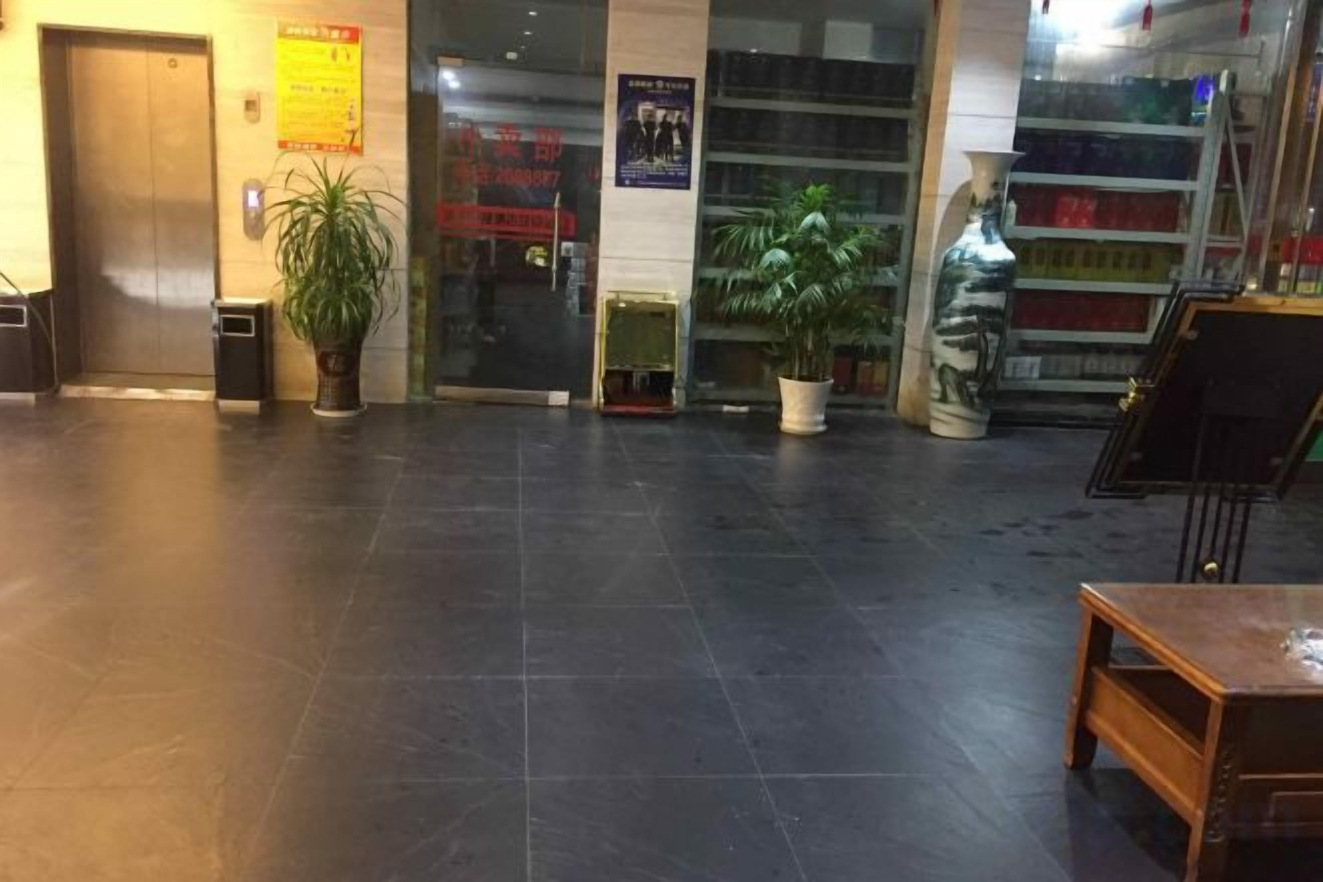 Vestíbulo con mostrador de recepción, plantas en macetas y puerta de vidrio.