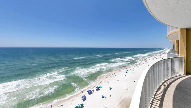 A beach view from a balcony with a railing, ocean waves, and beach umbrellas.