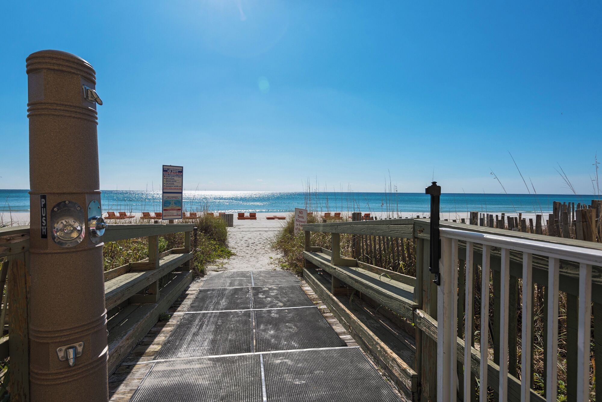 A wooden boardwalk leading to a beach with a lifeguard tower and a sign prohibiting tents.
