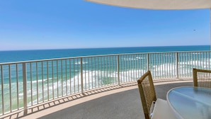 A balcony with a view of the ocean, a round table, and wicker chairs.