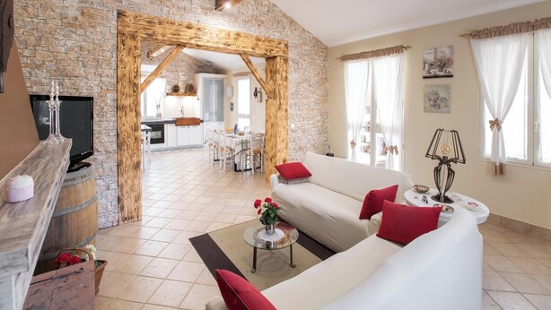 A spacious living room with a stone wall, wooden beams, a white sofa with red cushions, a coffee table, and a TV on a wooden stand. - 3888 Villetta tra Mari e Monti by Barbarhouse (San Giovanni Rotondo)