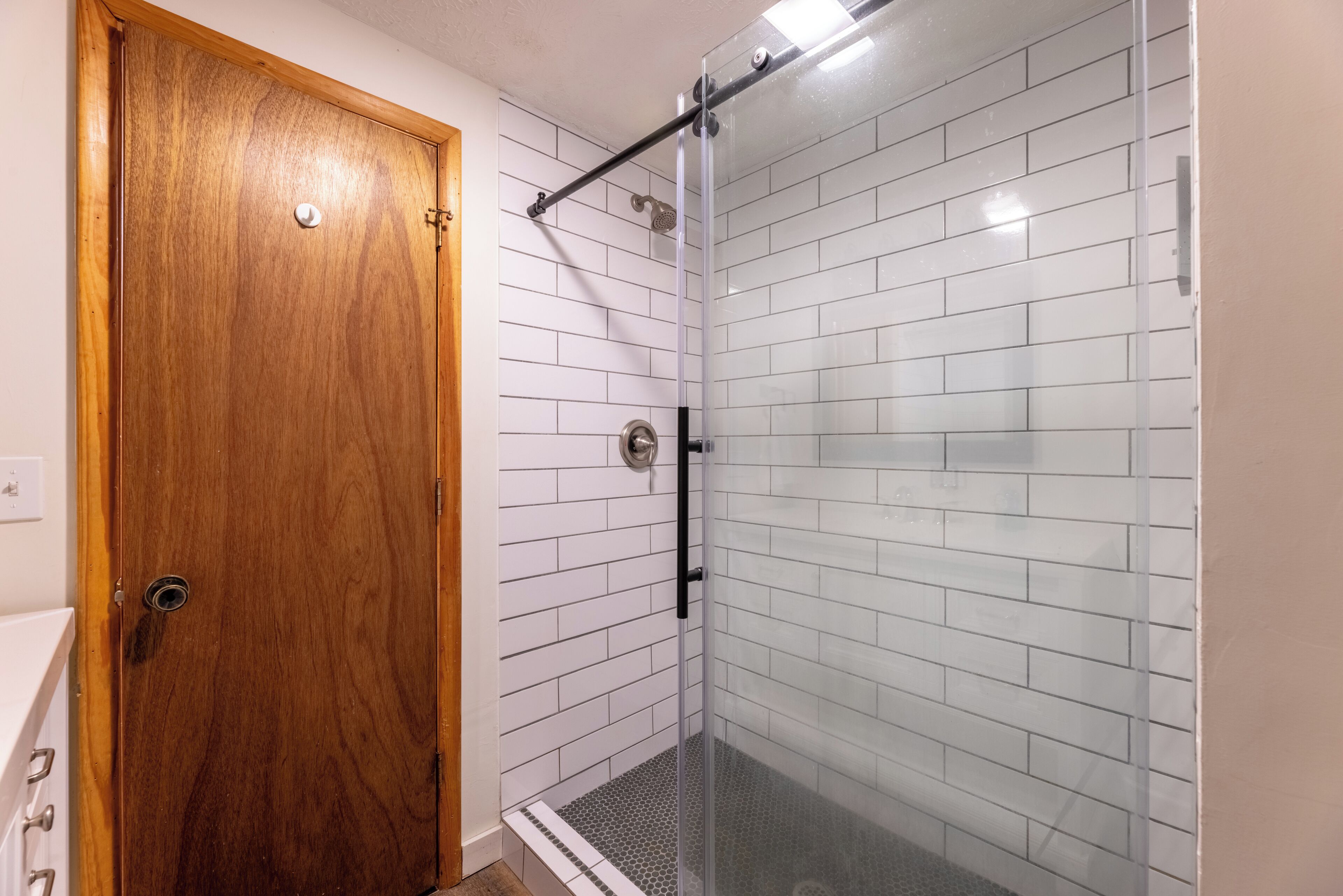 A bathroom with a wooden door, white tiled walls, and a glass shower enclosure.