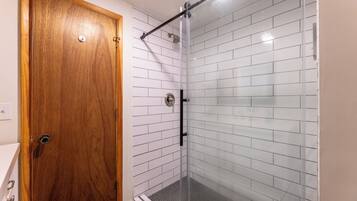 A bathroom with a wooden door, white tiled walls, and a glass shower enclosure.
