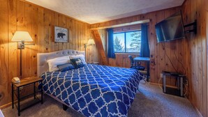 A wooden-paneled room with a bed, a desk, a TV, and a window with a view of trees. - Shamrock condo courtyard area features a bike wash rack, pickleball/tennis court, basketball court, covered pavilion, grills, firepit and playground!  Inside the condo there is space for everyone!  Ample parking and easy access to walking path. (Snowshoe)