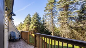 A wooden deck with a chair, surrounded by trees and a wooden railing. - Shamrock condo courtyard area features a bike wash rack, pickleball/tennis court, basketball court, covered pavilion, grills, firepit and playground!  Inside the condo there is space for everyone!  Ample parking and easy access to walking path. (Snowshoe)