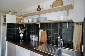 Uma cozinha com painel de parede escuro, prateleiras de madeira e uma pia de aço inoxidável.
