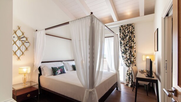 A four-poster bed with a canopy, bedside tables with lamps, a desk with a computer, and a patterned curtain. - Villa Francesca Relais (Gradara)