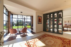 Una habitación amplia con ventanas grandes, una lámpara moderna, un tapete grande y una vitrina de cristal.