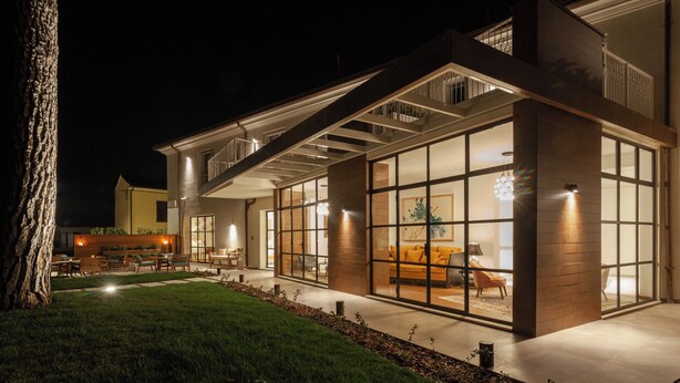 A modern house with large glass windows, a patio with outdoor furniture, and a well-lit interior. - Villa Francesca Relais (Gradara)